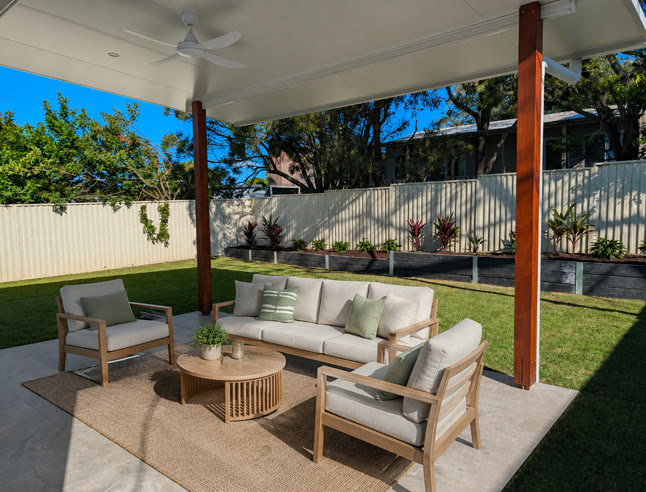 Covered outdoor living area with a ceiling fan, lounge seating and a level step out onto the lawn.